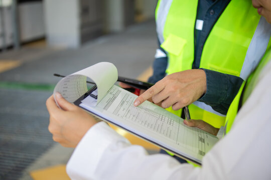 Inspection sheet being reviewed by two workers wearing safety vest in industrial environment showing detailed data and checklist for quality control and safety compliance - Powered by Adobe