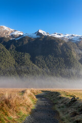 Scenery in South Island, New Zealand near Te Anau, with the snow capped Southern Alps and unpaved pathway into pasture lands and low lying fog