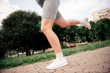 Active young woman jogging outdoors in a park, wearing stylish athletic wear, enjoying fitness and...