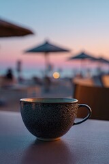 A muted blue teacup sits on a table at a beachside cafe, soft sunset colors in the background