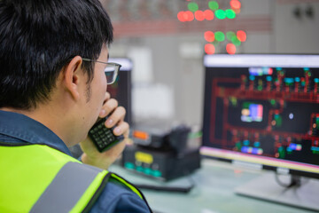 Engineer in high visibility vest is monitoring control systems in electricity room using computer and handheld radio
