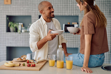 Multi-ethnic couple enjoying breakfast together in their modern kitchen, sharing a moment of happiness and connection