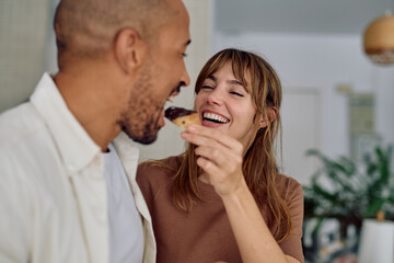 Smiling woman feeding her partner a delicious pastry, creating a warm and loving atmosphere in their home kitchen
