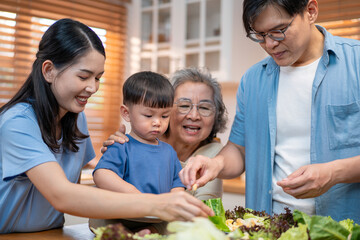 Asian multigenerational family enjoying mealtime in the kitchen with fresh vegetables. Grandmother warmly hugs the toddler while parents serve food, highlighting love, care, and healthy living.