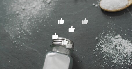 Tipping salt shaker spilling salt on kitchen countertop, with wooden spoon of salt, thumbs-up icons