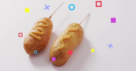 Featuring two battered corn dogs resting on white table, with mustard drizzles and geometric shapes
