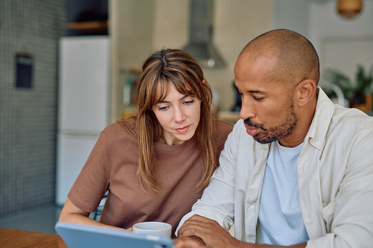 Interracial couple enjoying breakfast together in a cozy kitchen, using a tablet for browsing, sharing ideas, and connecting over coffee - Powered by Adobe