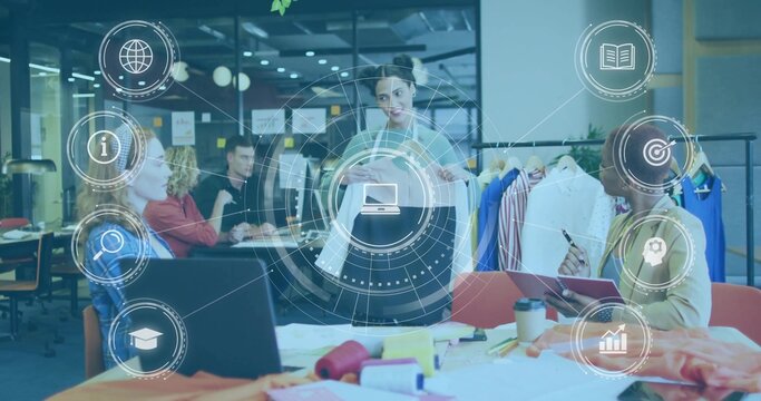 Lead designer wearing gray blazer presenting two garments in open-plan studio, with clothing rack
