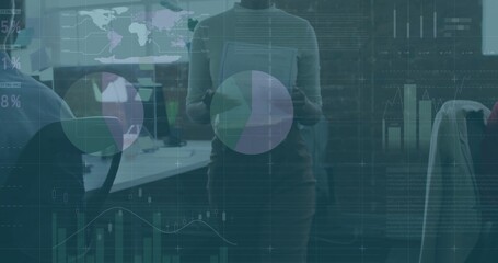 Presenting woman wearing suit holding tablet reviewing graphs in office, with monitors data overlay