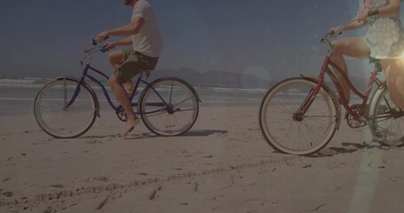 Cruising couple pedaling blue and red cruiser bikes along beach near water's edge, with ocean waves