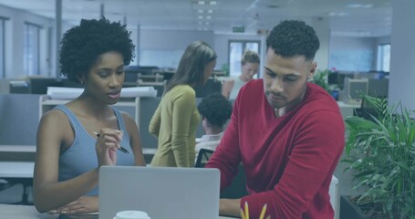 Collaborating coworkers reviewing laptop screen at open-plan office, with pen and desk plant