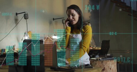 Speaking artisan woman holding smartphone and typing on laptop in workshop, with financial overlays