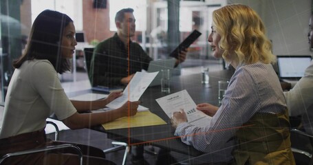 Office team sitting around glass conference table, with printed reports folder laptop water glasses