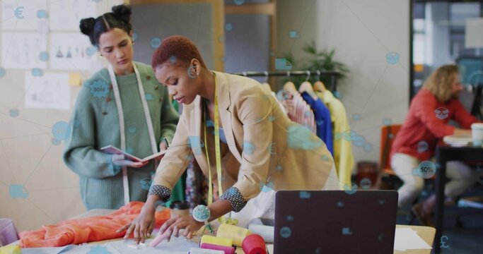 Collaborating designers leaning over worktable designing patterns in studio, with measuring tape