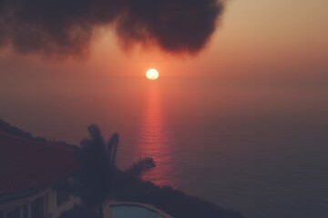 Fiery orange sun breaking through hazy clouds casting a dramatic light beam over silhouetted mountain peaks at sunset