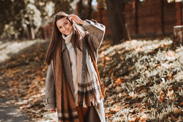 Young woman enjoying a sunny autumn day in a park, wearing a stylish coat, with colorful leaves and...