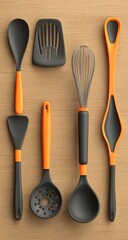 Colorful, modern kitchen utensils on a light-wood surface.  Six pieces in black and orange.  Spoons, spatula, whisk, and slotted spoon.  Geometric shapes.  Top-down view