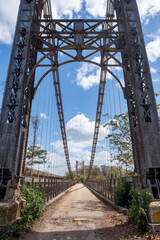 A dramatic low-angle view of a historical steel bridge in Venezuela. The old suspension bridge,...