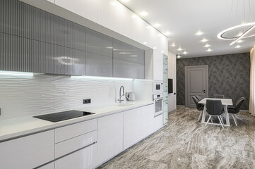Modern kitchen with white cabinets, gray accents, and a dining area featuring a white table and...