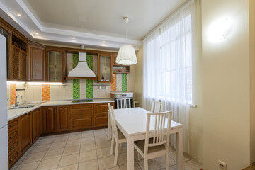 well-lit kitchen features wooden cabinets, a white dining table with chairs, tiled flooring and backsplash, and a window with sheer curtains