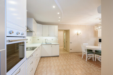 Bright kitchen with white cabinets, tile floor, and dining area. Oven and sink visible.  Warm, inviting space