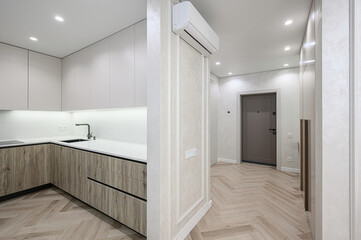 modern, bright interior featuring a kitchen area with sleek cabinetry and a hallway with a herringbone floor. The color palette is neutral with a touch of wood texture
