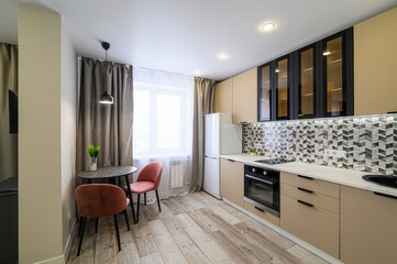 modern kitchen features beige cabinets, black accents, a dining table with two pink chairs, wood-look floors, and geometric backsplash tiles