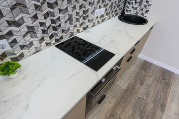 modern kitchen detail features a white marble countertop with an integrated black stovetop and...