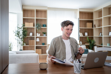 Fototapeta premium Freelancer smiling and working from home using laptop and reading documents