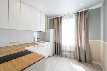 Bright kitchen with white cabinets, wood countertop, and light-filled window with curtains