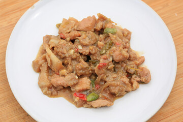 Stir-fried pork with shrimp paste and stink bean in white plate on bamboo wooden board background.