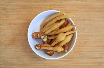 Finger root or Chinese ginger in white bowl on bamboo wooden background, preparation process for cooking. Top view.