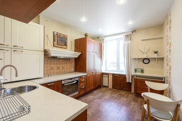 Cozy kitchen with white & wood cabinets, light countertops, a window, and dining area. Warm lighting, shelves with decor