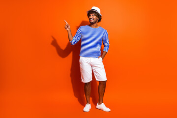 Smiling young man wearing a striped sailor shirt poses against a bright orange background in a...