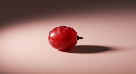 Single red grape rests on a pale pink surface under a focused spotlight, creating a simple yet elegant still life with a minimalist aesthetic.