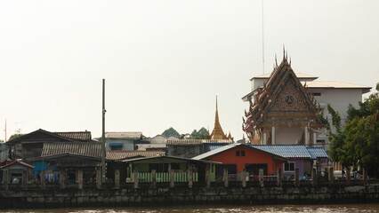 Naklejka premium On the Chao Phraya River pier in a neighborhood of Bangkok, Thailand, the Tai pagoda with golden details stands out among the condominiums