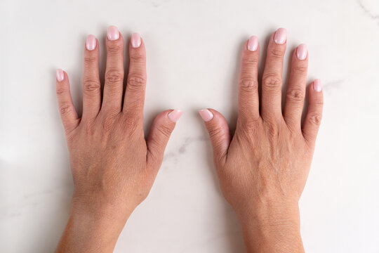 Top view of two mature female hands with clean pink manicure on white marble surface. Perfect for dermatology, skincare, beauty and aging-related content.