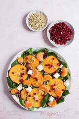 Winter salad. Fresh persimmon and citrus salad with spinach, feta, and pomegranate on pink table. 