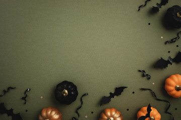 Halloween party background from orange and black pumpkins, bats on dark green table top view. Happy halloween holiday greeting card, flat lay.