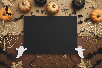Halloween party composition with empty black card with festive decoration from pumpkins, bats, spider web, ghosts on golden background top view.