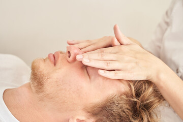 Young caucasian male relaxing during facial massage therapy at spa session.