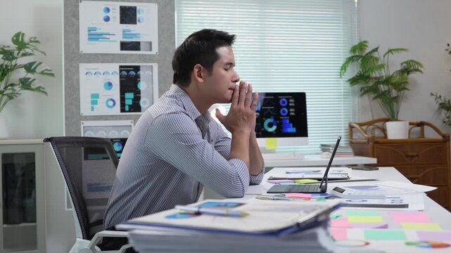 Exhausted corporate professional leaning over laptop, showing intense concentration during high pressure work moment with scattered documents surrounding workspace