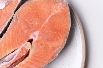 Close-up of raw salmon steak on white plate. High-protein seafood concept for healthy meal preparation, restaurant menu design, cooking blogs, and nutrition content.