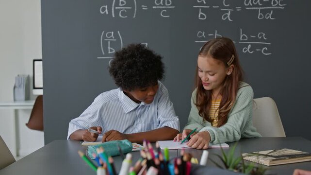 Young African American boy and Caucasian girl diligently working on math problems together during algebra class in school