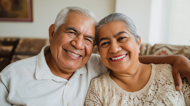 portrait of happy and smiling senior Hispanic couple embracing and sitting on living room sofa - Powered by Adobe