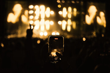 Filming on smartphone the concert among the crowd of people. Enjoying music concert in front of bright stage lights.