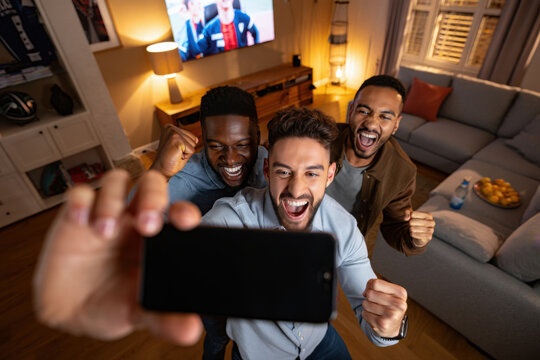 Excited male friends taking selfie while watching sports on tv