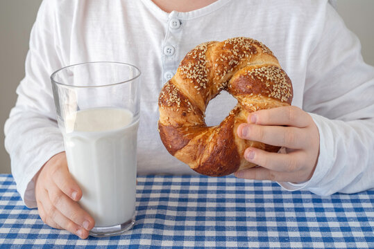 Glass of milk and Beigel in the hands of a child for tasty breakfast.