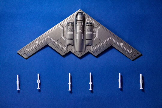 Top view of a B-2 Spirit stealth bomber scale model displayed on a blue surface with five missiles arranged below. The iconic flying wing design represents modern aviation, stealth technology
