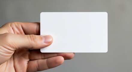 A hand holding a blank white card against a neutral gray background, ready for text.
